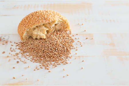 Wheat grains with piece of bread on white wooden background
