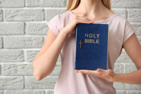 Religious young woman with Bible against brick wallの写真素材