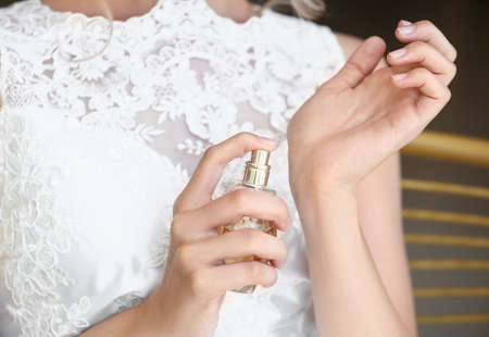 Beautiful young bride with bottle of perfume indoors, closeup
