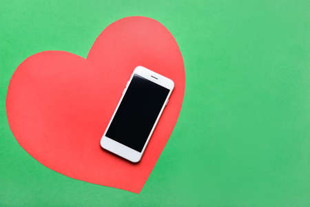 Modern mobile phone and paper heart on color backgroundの写真素材