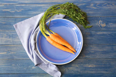 Plate with fresh carrots on wooden table