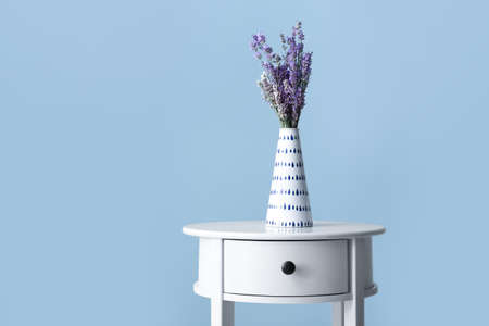Beautiful lavender flowers in vase on table against color backgroundの写真素材