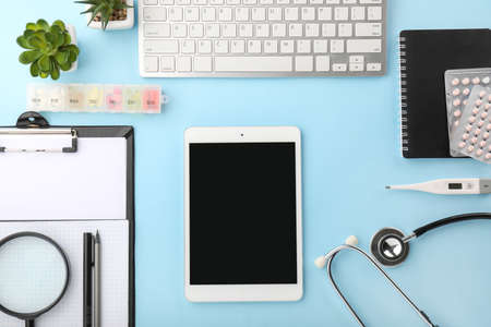 Tablet computer, clipboard, pills, stethoscope and PC keyboard on color background
