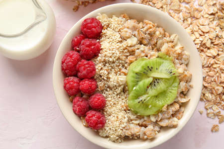 Bowl with tasty sweet oatmeal and milk on light table