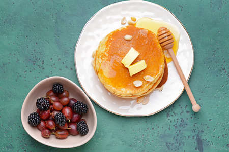 Tasty pancakes with butter and berries on color background
