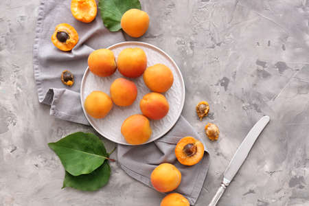 Plate with tasty apricots on gray background