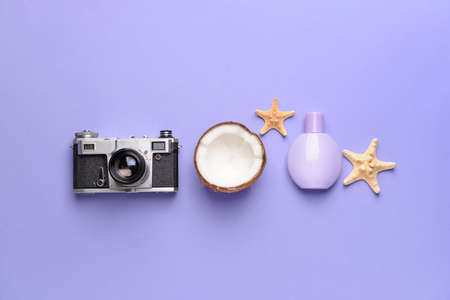 Photo camera, perfume, coconut and starfish on color background