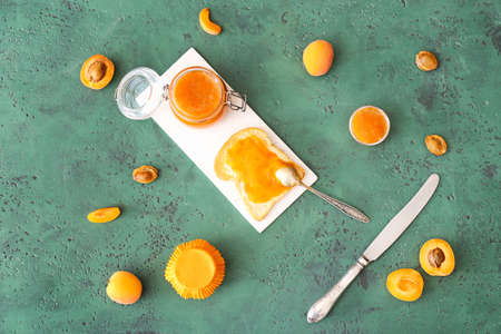 Tasty apricot jam with slice of bread on color backgroundの写真素材