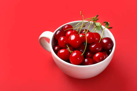 Cup with ripe sweet cherry on color backgroundの写真素材