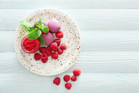 Plate with fresh raspberries, jam and macarons on white wooden tableの写真素材