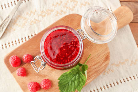 Jar of tasty raspberry jam on table