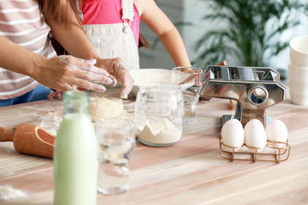 Mother with little daughter kneading dough together in kitchenの写真素材