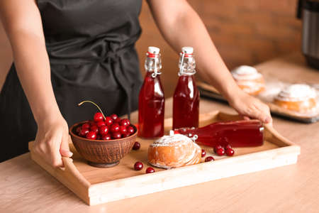 Woman with tasty cherry juice and sweet bun on tray at table