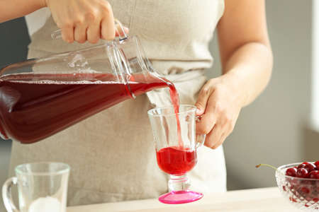 Woman pouring tasty cherry juice from jug into glass cup