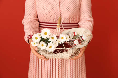 Woman holding basket with bottles of tasty cherry juice and flowers on color backgroundの写真素材