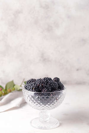 Glass bowl with tasty blackberries on light tableの写真素材