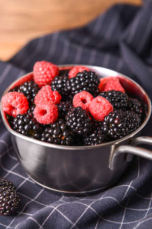 Pot with tasty blackberries and raspberries on tableの写真素材