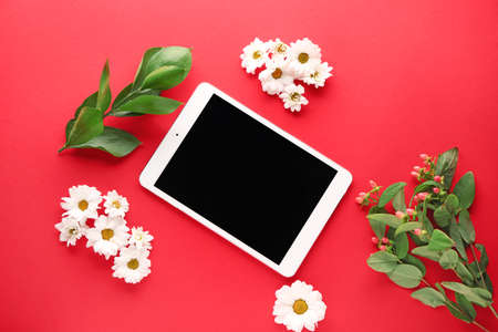 Modern tablet computer with flowers and leaves on color background