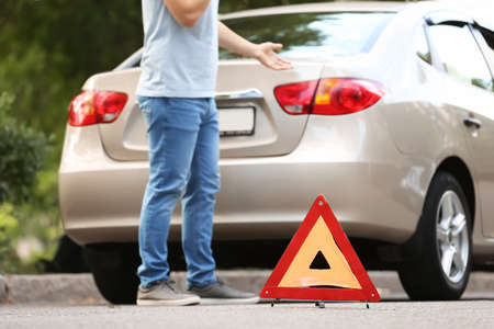 Man calling his insurance agent while standing near broken car on road