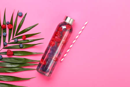 Bottle of fresh infused water and tropical leaf on color background