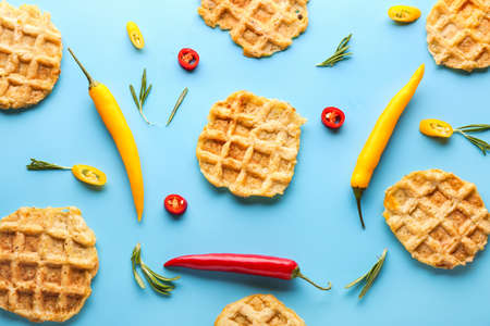 Tasty waffles with chili peppers and herbs on color background