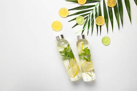 Bottles of fresh infused water, tropical leaf and citrus fruits on white background