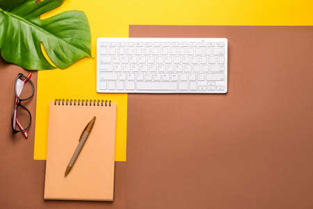 Modern computer keyboard with stationery and eyeglasses on color background