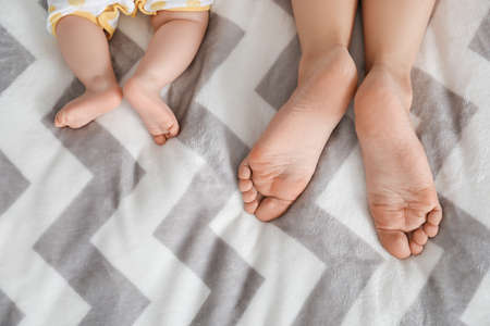 Feet of mother and cute little baby lying on bedの写真素材
