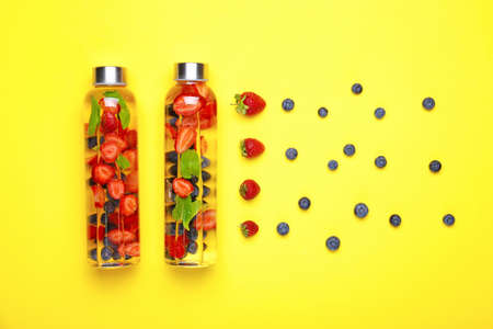 Bottles of tasty infused water and berries on color background