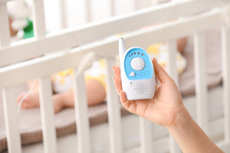 Female hand with modern baby monitor and little sleeping child on background