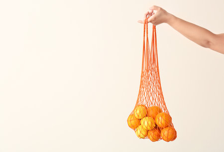 Female hand holding mesh eco bag with fruits on light backgroundの写真素材