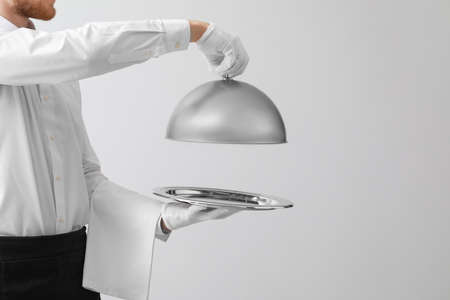 Handsome waiter with tray and cloche on light background