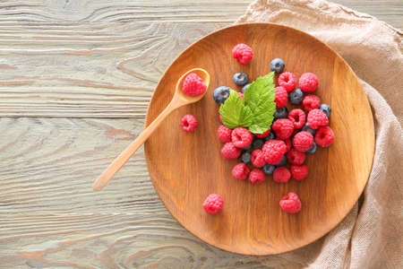 Plate with tasty ripe berries on wooden table