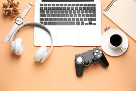 Laptop with joypad, headphones and cup of coffee on color background