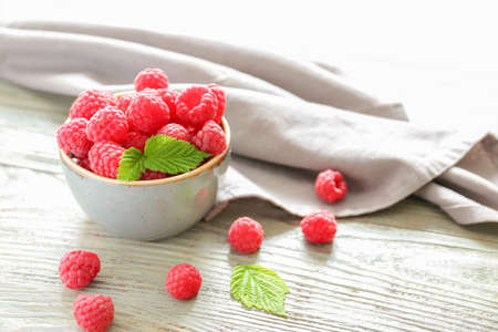 Bowl with tasty ripe raspberries on wooden table