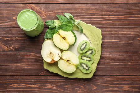 Glass of fresh healthy smoothie and plate with cut fruits on wooden backgroundの写真素材