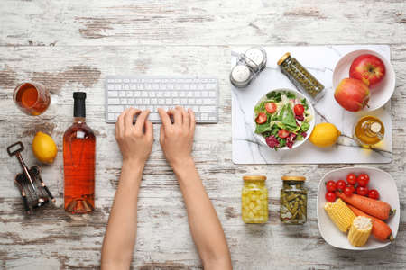 Hands of female food blogger with computer keyboard, wine and products on wooden backgroundの写真素材