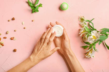 Female hands with natural cream on color background