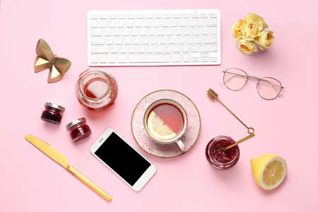 Computer keyboard with mobile phone, products and cup of tea on color background