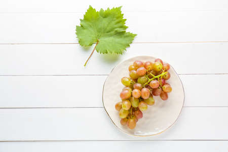 Plate with tasty sweet grapes on white wooden tableの写真素材