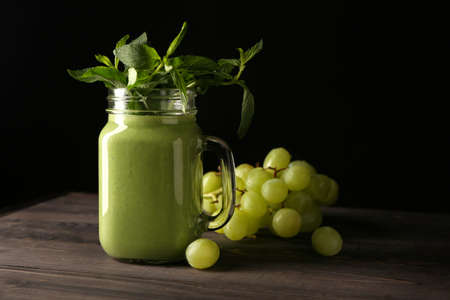 Mason jar of tasty smoothie with ingredients on table against dark backgroundの写真素材