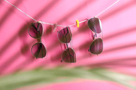 Stylish sunglasses hanging on rope against color background, view through tropical leafの写真素材