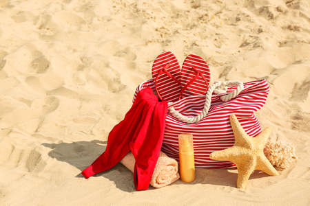 Bag with flip-flops, swimsuit, towel and cosmetics on sand beachの写真素材