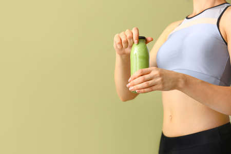 Sporty woman with bottle of tasty green smoothie on color backgroundの写真素材