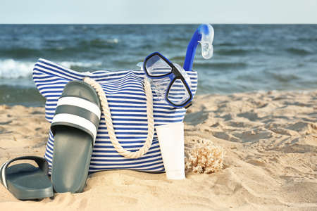 Bag with flip-flops, set or snorkeling and cosmetics on sand beachの写真素材