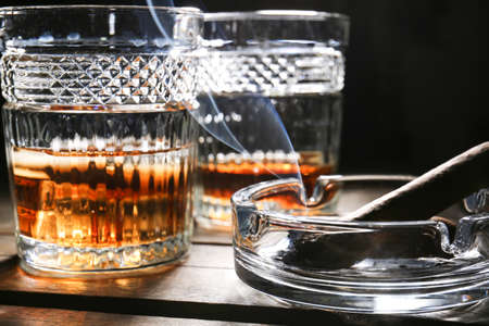 Glasses of cold whiskey with cigar on wooden table