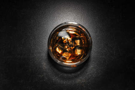 Glass of cold whiskey with ice on dark tableの写真素材