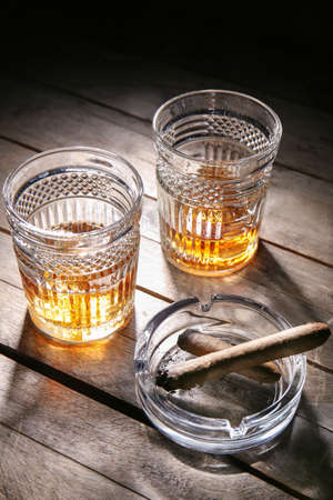 Glasses of cold whiskey with cigars on wooden tableの写真素材