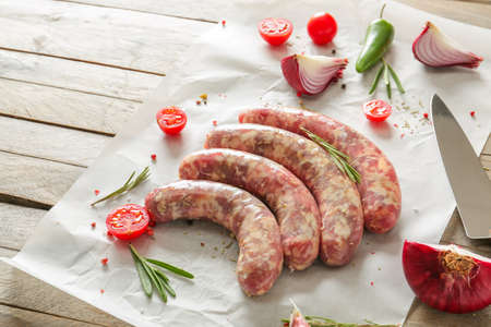 Fresh raw sausages with herbs, spices and vegetables on tableの写真素材