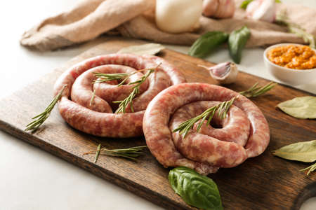 Wooden board with fresh raw sausages and herbs on tableの写真素材
